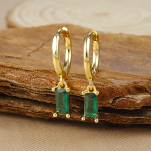Macro detail of gold hoop earrings with emerald-cut green zircon on wood texture