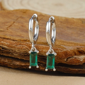 Close-up of silver hoop earrings with rectangular emerald zircon charms on wood