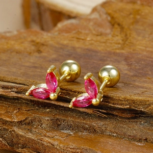 Macro shot of gold-plated stud earrings featuring red zircon marquise petals on wood background