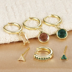Detailed close-up of gold earrings set with emerald and warm-toned gemstones on fabric