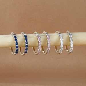 Detalle de pendientes de aro plateados con circonitas azules, rosas y blancas engastadas