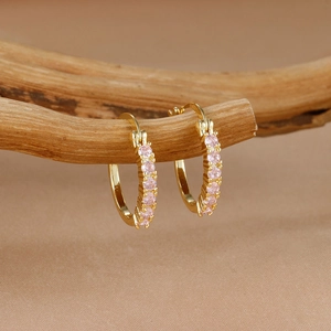 Elegantes pendientes de aro dorados con pequeñas circonitas rosas en una rama