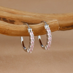 Primer plano de aretes de aro plateados con cristales rosas sobre una rama de madera