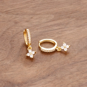 Détail de boucles d'oreilles trèfle dorées avec cristaux sur un fond en bois rustique