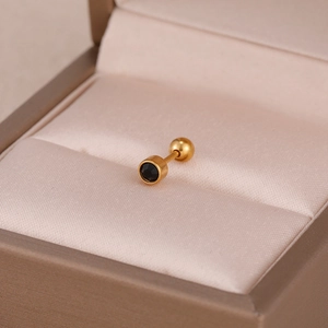 Gros plan d'une boucle d'oreille dorée avec cristal noir sur tissu de soie rose