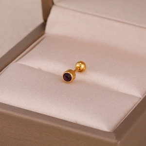 Détail d'un clou d'oreille doré avec zircon violet sur velours champagne