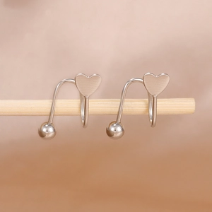 Minimalist silver heart and bead spiral earrings displayed on a rustic wooden stand