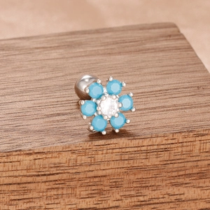 Gros plan détaillé d'une boucle d'oreille fleur argentée avec pierres bleu ciel