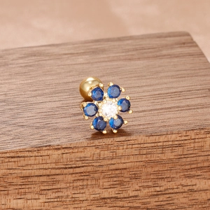 Gros plan d'une boucle d'oreille fleur dorée avec gemmes bleues et fermoir à boule