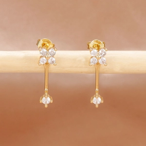 Detalle de pendientes dorados con flores de circón colgados en soporte de madera