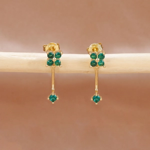 Vista macro de pendientes de flores doradas con circonitas verdes en soporte