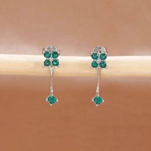 Primer plano de pendientes de trébol de cuatro hojas con piedras verdes en soporte de madera