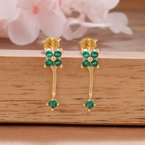 Detalle de pendientes de flores doradas con circonitas verdes sobre raso champán