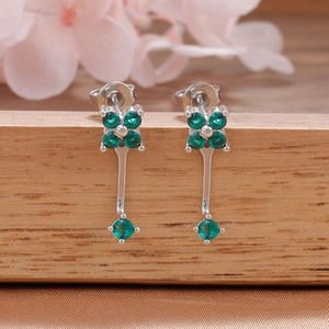 Detalle de pendientes de trébol plateados con circonitas verdes en soporte de madera