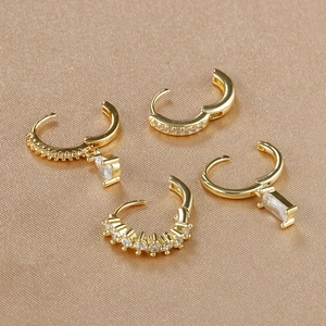 Close-up of four gold zircon earrings featuring rectangle and teardrop pendants on satin