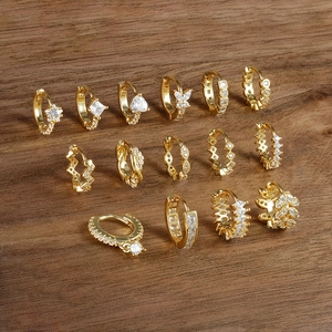 Collection of tiny gold earrings with cubic zirconia charms on a dark wood background