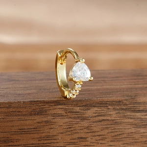 Close-up of golden hoop earring with heart-shaped zircon on a dark wood stand