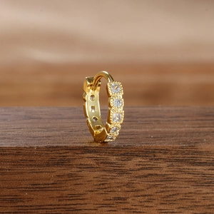 Macro detail of gold hoop earring with four round cubic zirconia and beaded edge texture