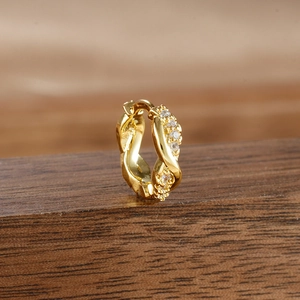 Close-up of twisted gold earring with micro-pave cubic zirconia on a wooden base