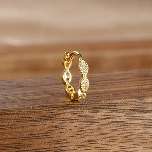 Close-up of golden huggie earring with micro-pave white stones on a wooden stand