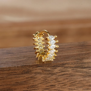 Detail of gold huggie earring featuring marquise-cut cubic zirconia on a wooden surface