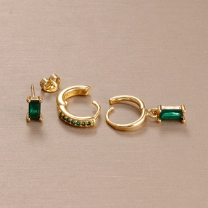 Detailed set of gold earrings with emerald green stones on textured background