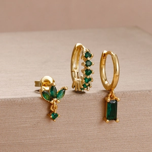 Detailed macro view of gold flower earrings set with emerald green crystals and charms
