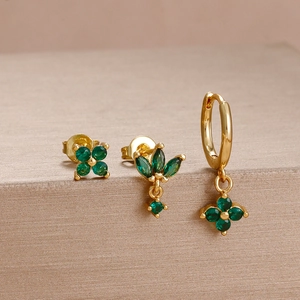 Detailed macro view of gold flower earrings set with faceted deep green gemstones
