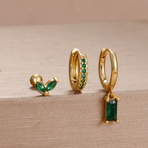 Close-up of gold earrings set with green stones and elegant leaf pattern details