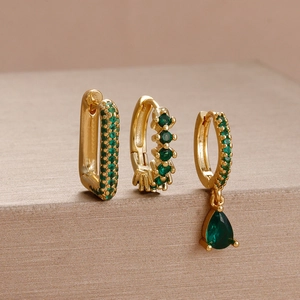 Detail of three-piece gold flower earrings set with green gemstones in a macro luxury display