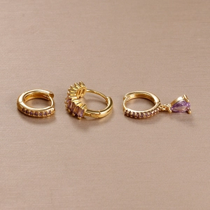 Detailed view of three gold-plated earrings set with purple crystals and pear pendant