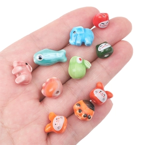 Macro shot of colorful handmade ceramic fish and animal beads held in hand for scale