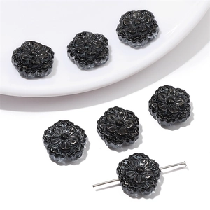 Detalle de cuentas de flores negras de 15mm para joyería DIY sobre cerámica blanca