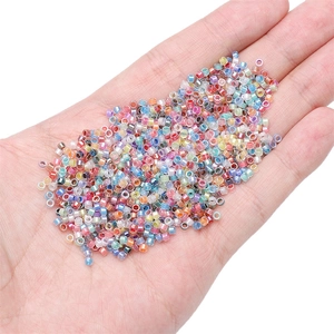 Macro detail of mixed colorful 2.5mm glass seed beads held in hand for size perspective