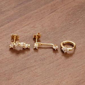 Dettaglio del set di tre orecchini dorati con zirconi incastonati su fondo in legno
