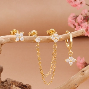 Detail of gold floral tassel earrings and zircon studs displayed on a natural wooden branch