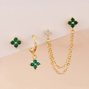 Close-up of gold floral earrings set with green stones and hanging chain details