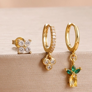 Makroansicht goldener Blumenohrringe und Ananas-Creolen-Set mit Kristallsteinen