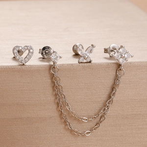 Détail de boucles d'oreilles argentées avec cœur, papillon et clous à chaîne fleurie