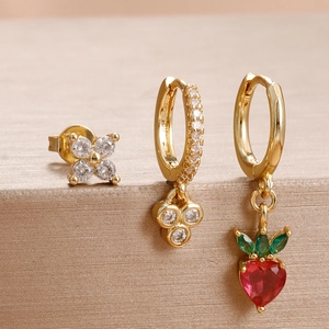 Vue macro de boucles d'oreilles dorées avec clou fleur en zircon et pendentif fraise