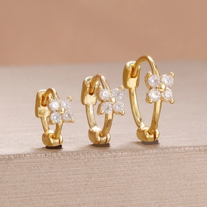 Vue macro de trois boucles d'oreilles fleurs dorées serties de zircons blancs