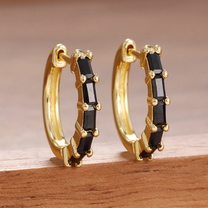 Gros plan détaillé de boucles d'oreilles huggie dorées avec incrustations noires rectangulaires