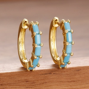 Détail de créoles dorées ornées de pierres turquoise en taille baguette avec griffes