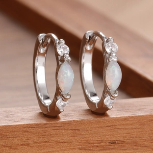 Macro detail of silver marquise opal earrings with zircon accents on wood background