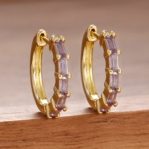 Détail de boucles d'oreilles dorées avec zircons violets rectangulaires sur bois