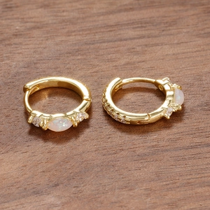 Macro shot of gold hoop earrings featuring marquise opal and zircon on wood surface