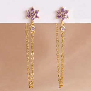 Dettaglio di orecchini a nappa dorati con pietre a fiore viola e catena pendente