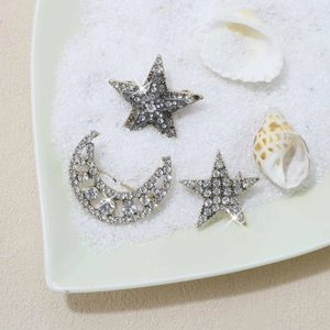Detail of crescent moon and star brooches with rhinestones on a sand and shell background