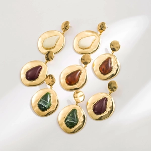 Close-up of geometric gold drop earrings with colorful resin stones in ivory and green