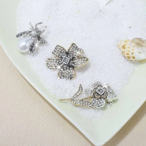 Detailed view of rhinestone-encrusted flower and bee brooches on white pebbles